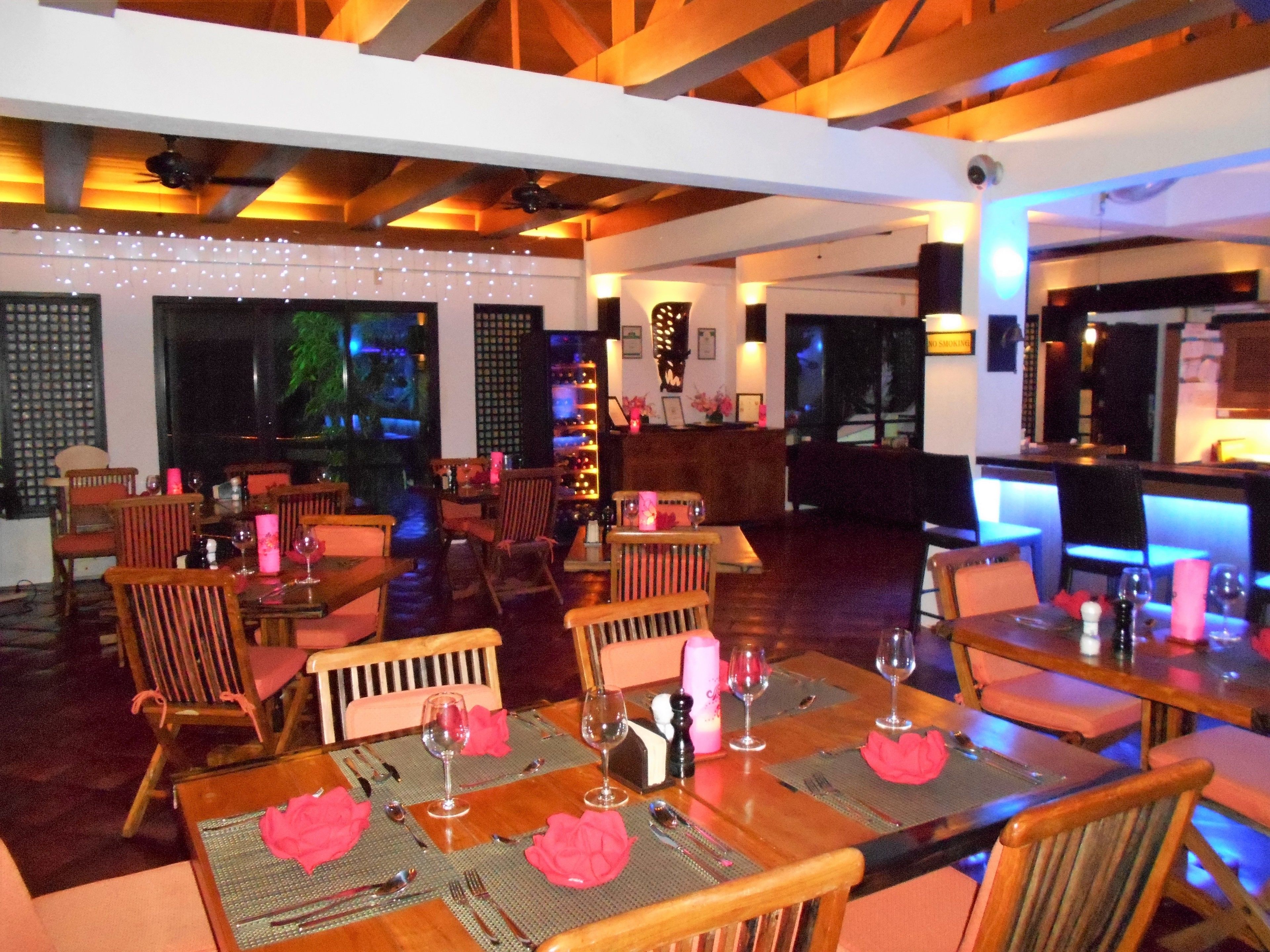 A restaurant with wooden tables and chairs, string lights, and a bar area.