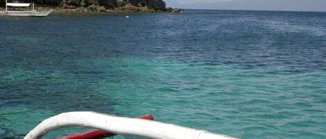 A boat with a red and white structure, clear turquoise water, and a rocky cliff in the background.