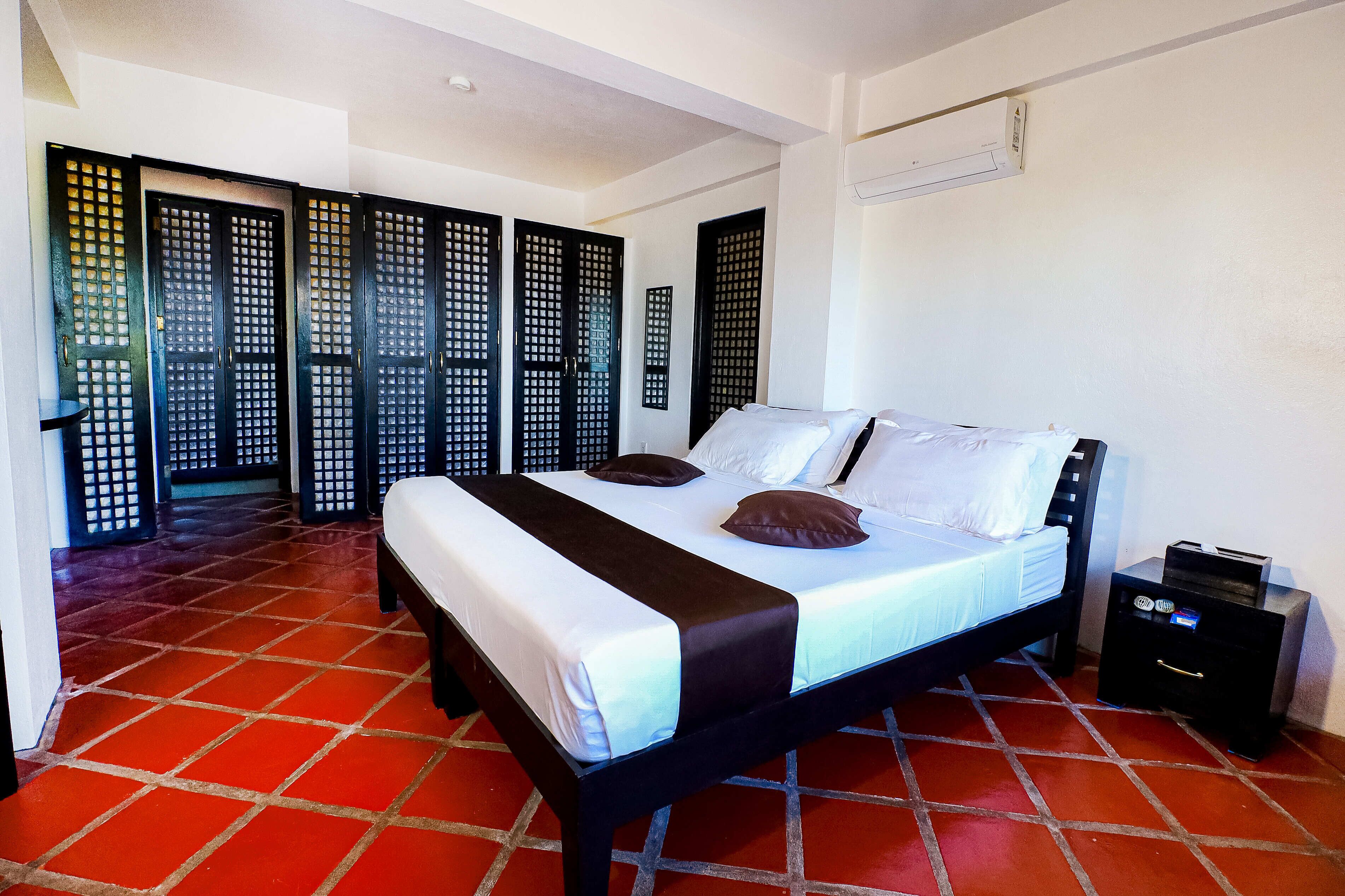 A bedroom with a bed, a nightstand, and a red-tiled floor.