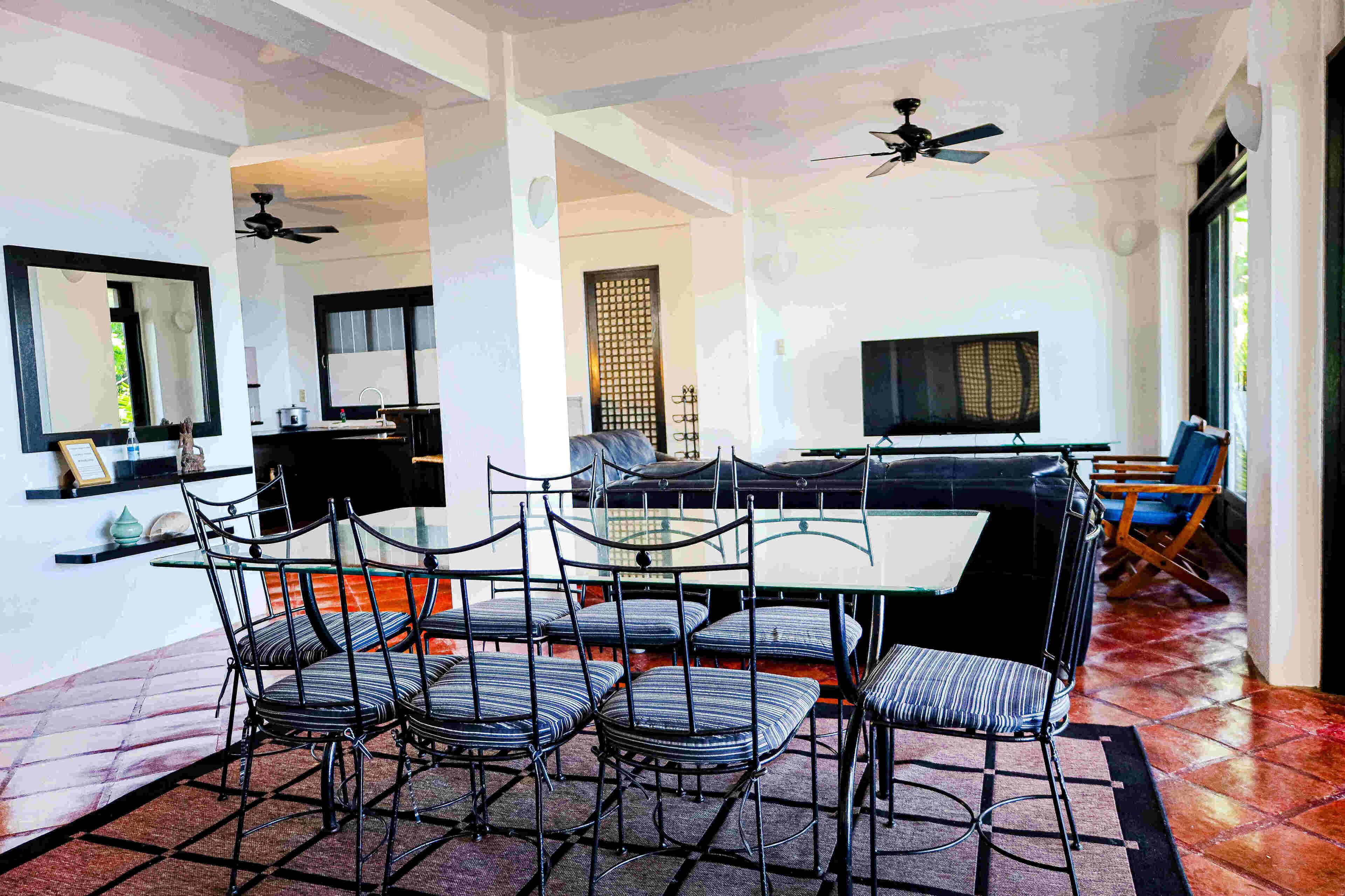 A dining area with a glass table and metal chairs, a TV, and a ceiling fan.