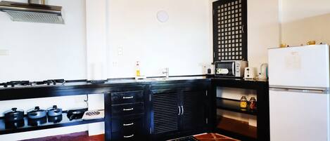 A kitchen with a black countertop, white refrigerator, and a red-tiled floor.