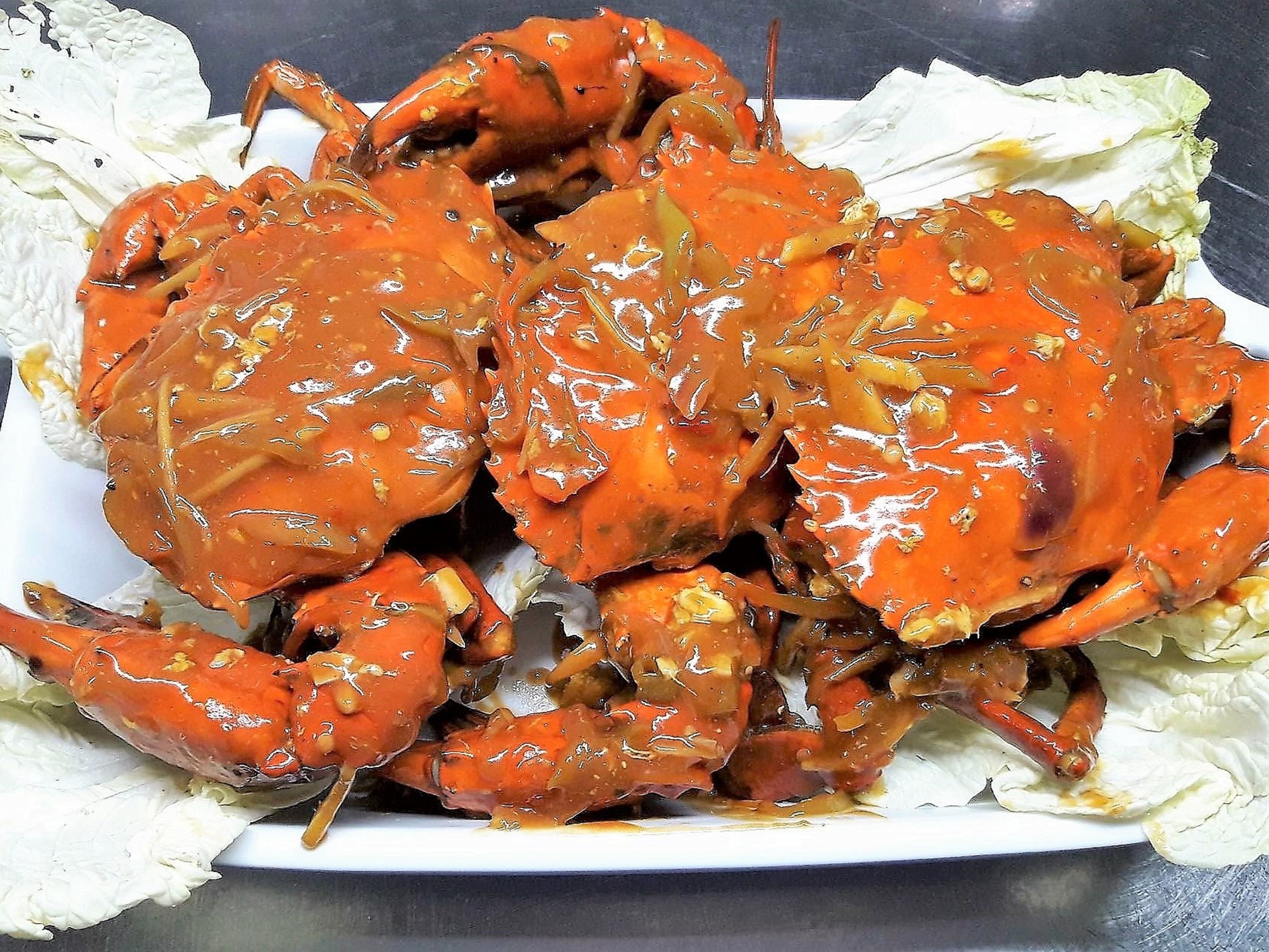 A plate of cooked crabs with a glossy sauce, served on a white plate with lettuce leaves.
