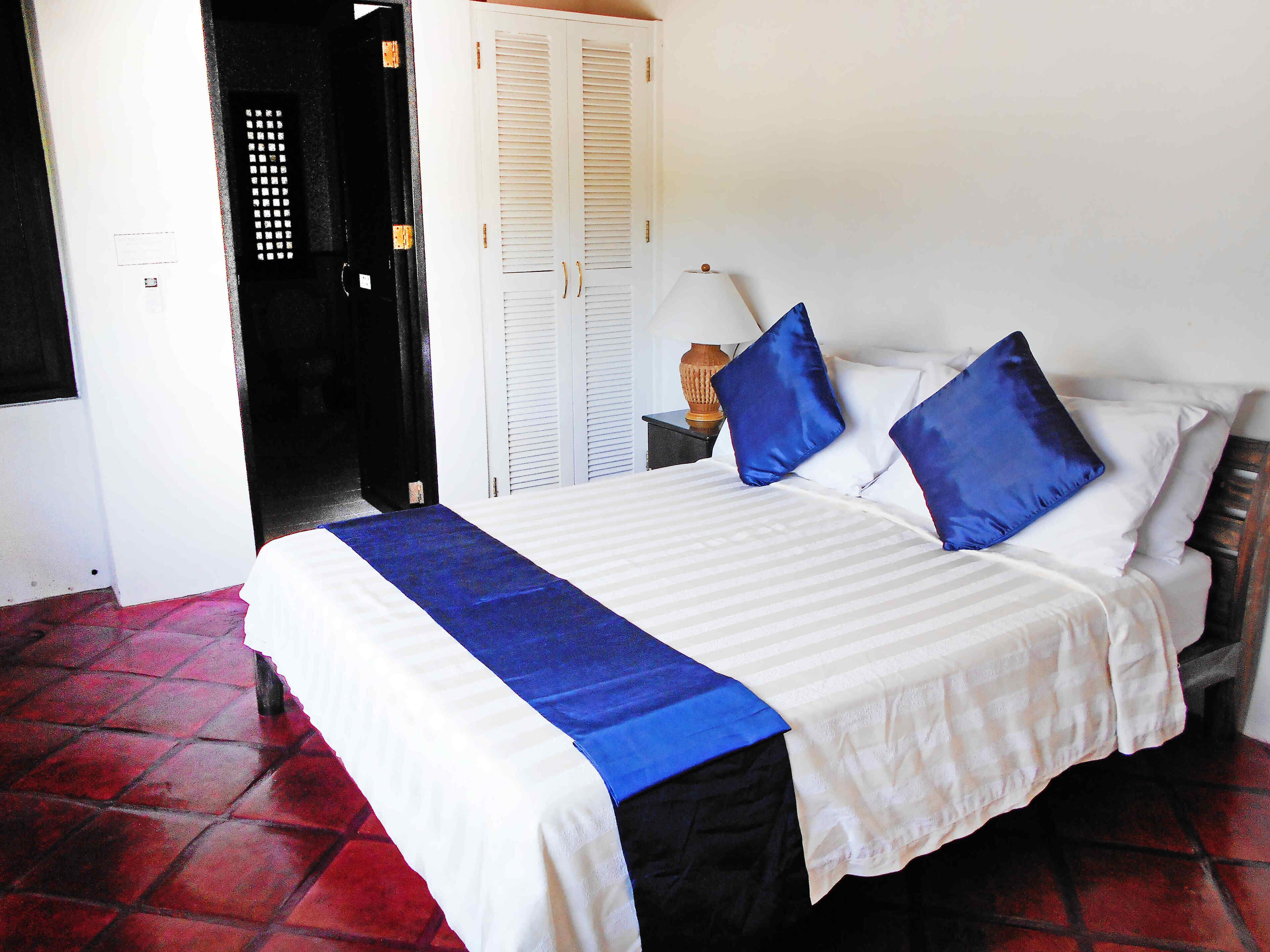 A bed with white and blue bedding, a lamp on a bedside table, and a door with a window.