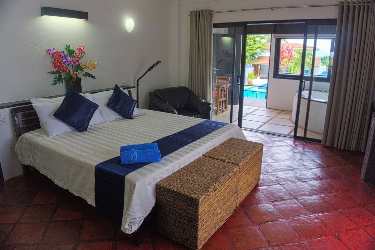 Hotelkamer met een bed, een bankje, een stoel, een klein tafeltje, een vaas met bloemen en uitzicht.