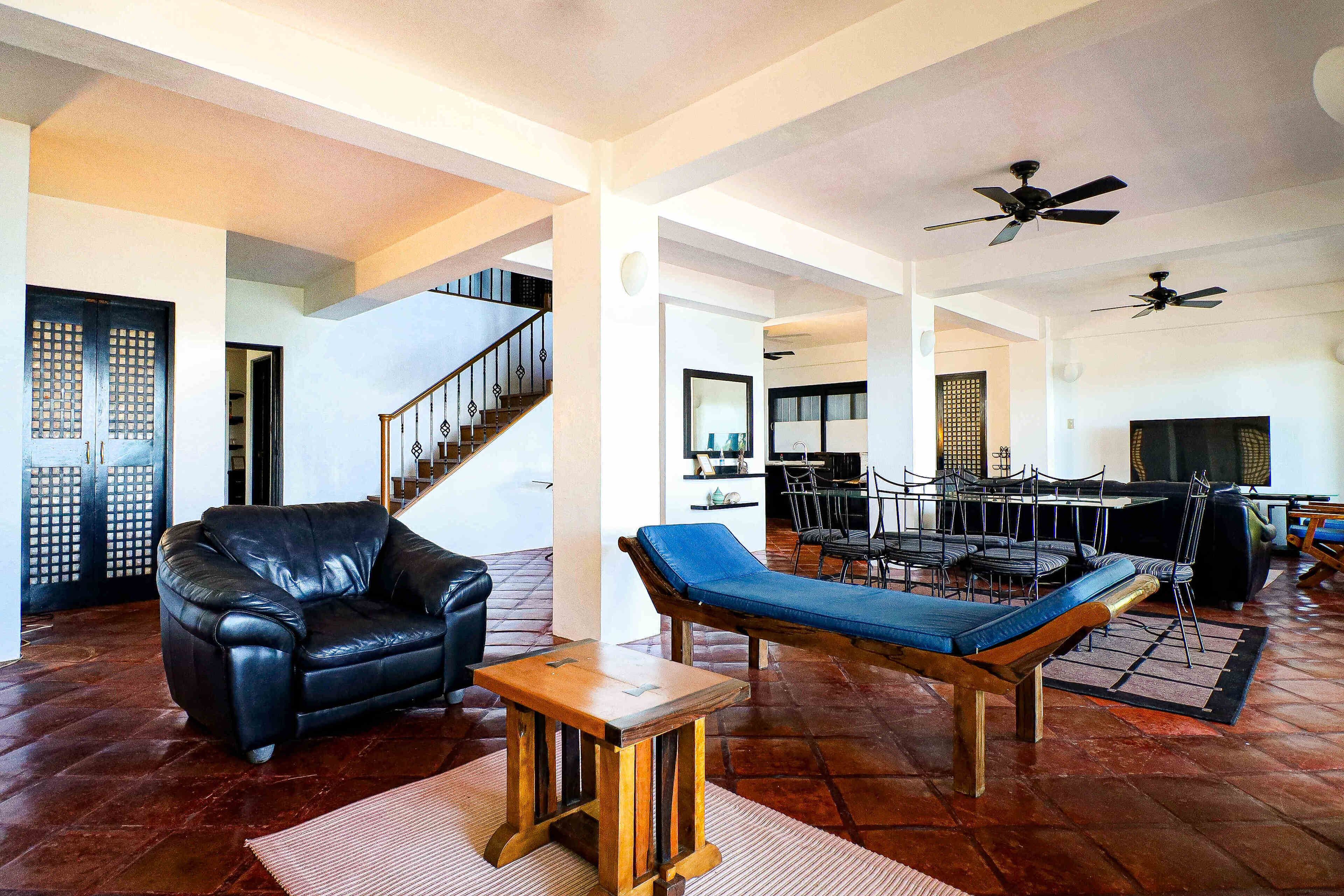 A spacious living area with a leather sofa, a wooden coffee table, and a blue cushioned bench. A staircase with a railing leads to another level.