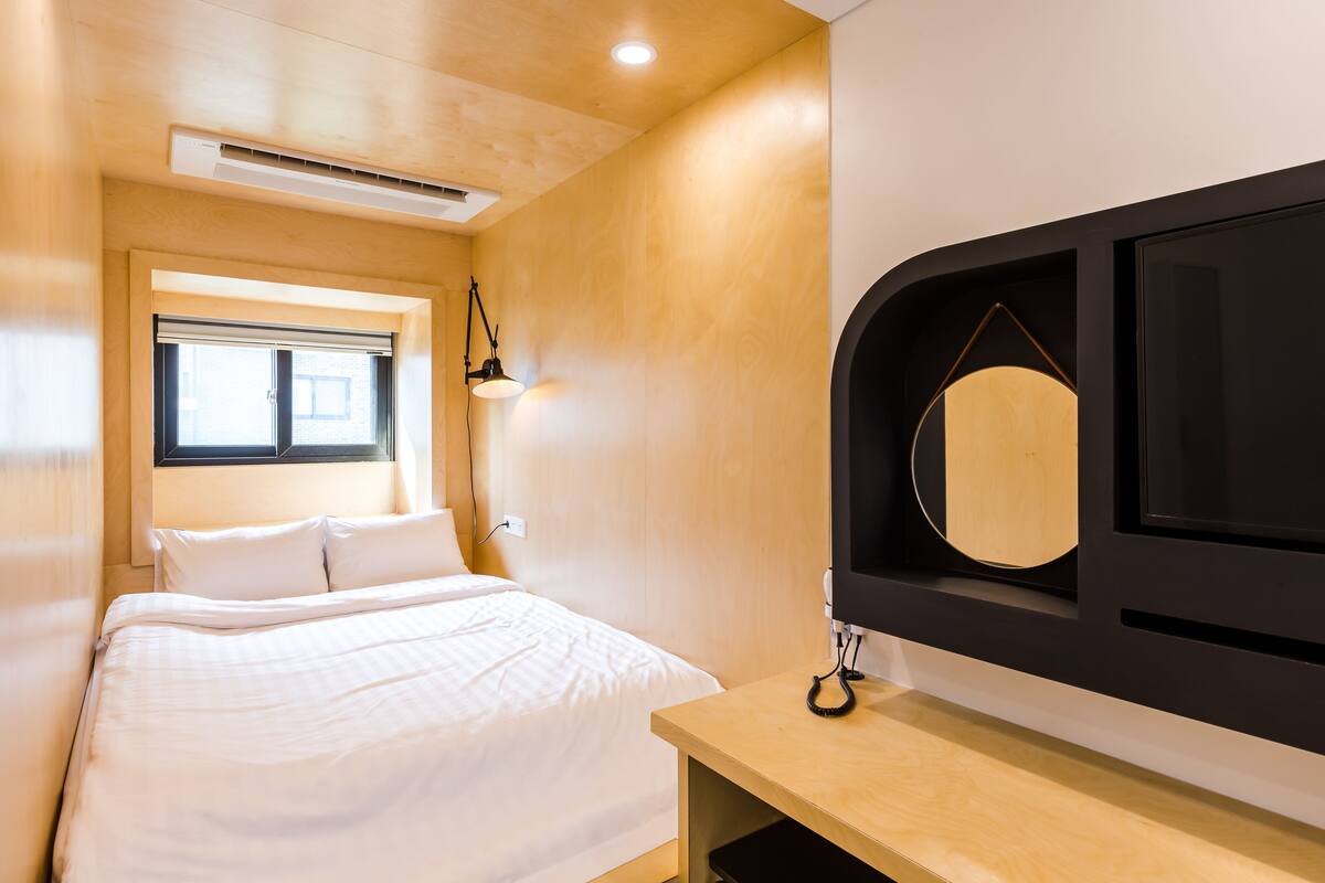 A bedroom with a bed, a window, a desk, and a television.