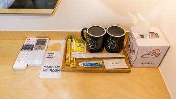 A hotel room's amenities tray with a remote control, a tissue box, two mugs, a bar of soap, and a tray with toiletries.