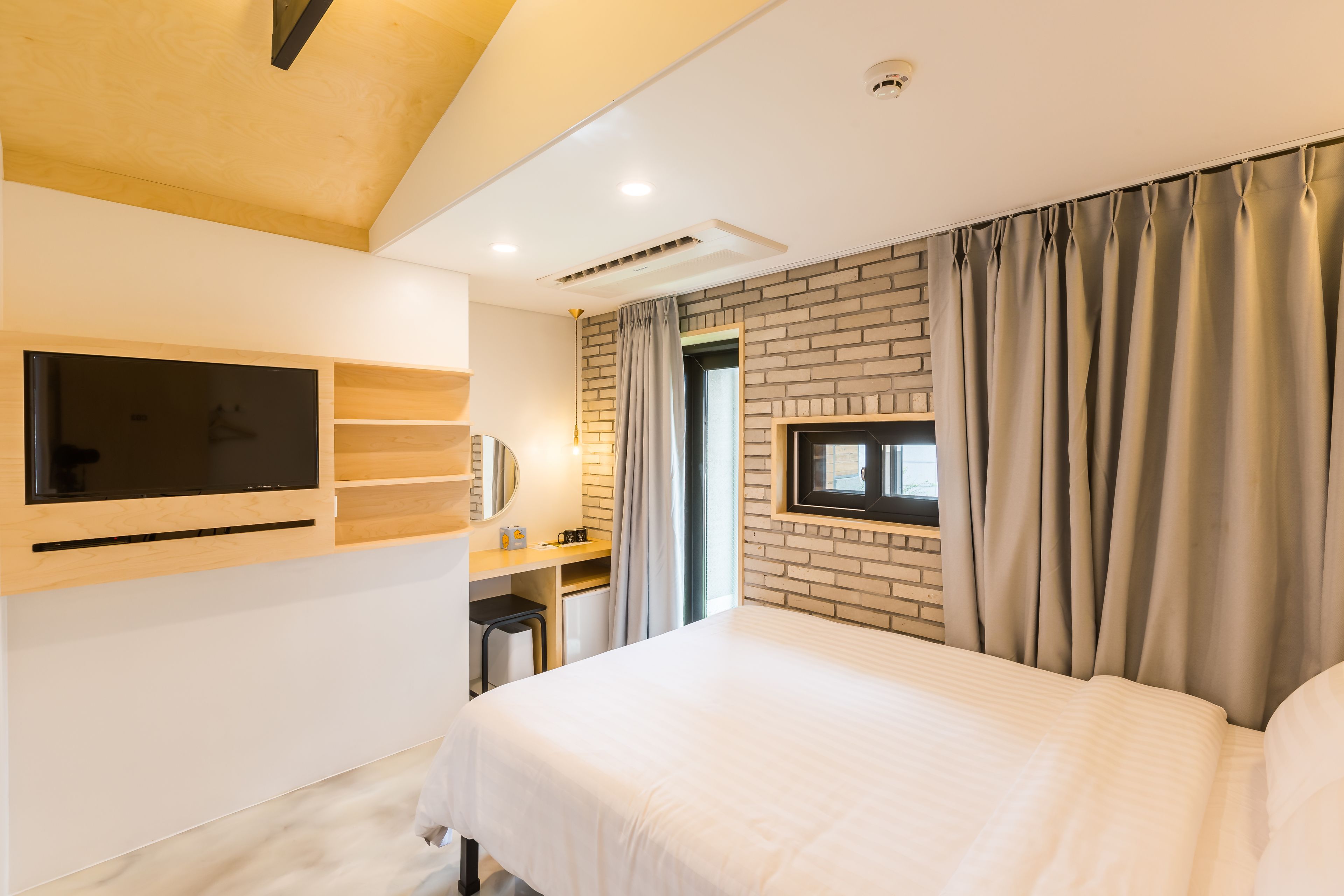 Ein modernes Hotelzimmer mit einem großen Bett, einem an der Wand montierten Fernseher, einem kleinen Schreibtisch und einer Wand mit Ziegeln.