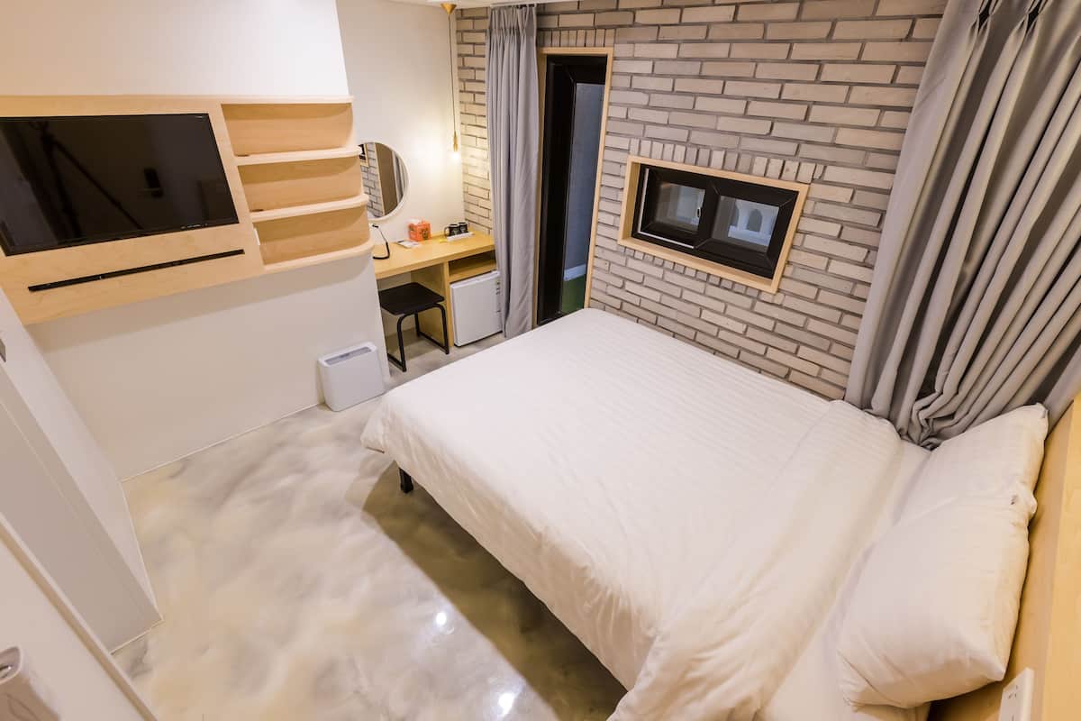 A hotel room with a bed, a desk with a computer, a TV, and a small fridge.
