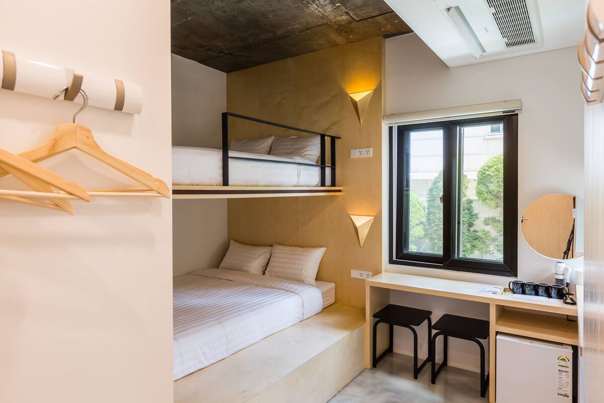 A bunk bed room with a desk, a mirror, and a window with a view of trees.