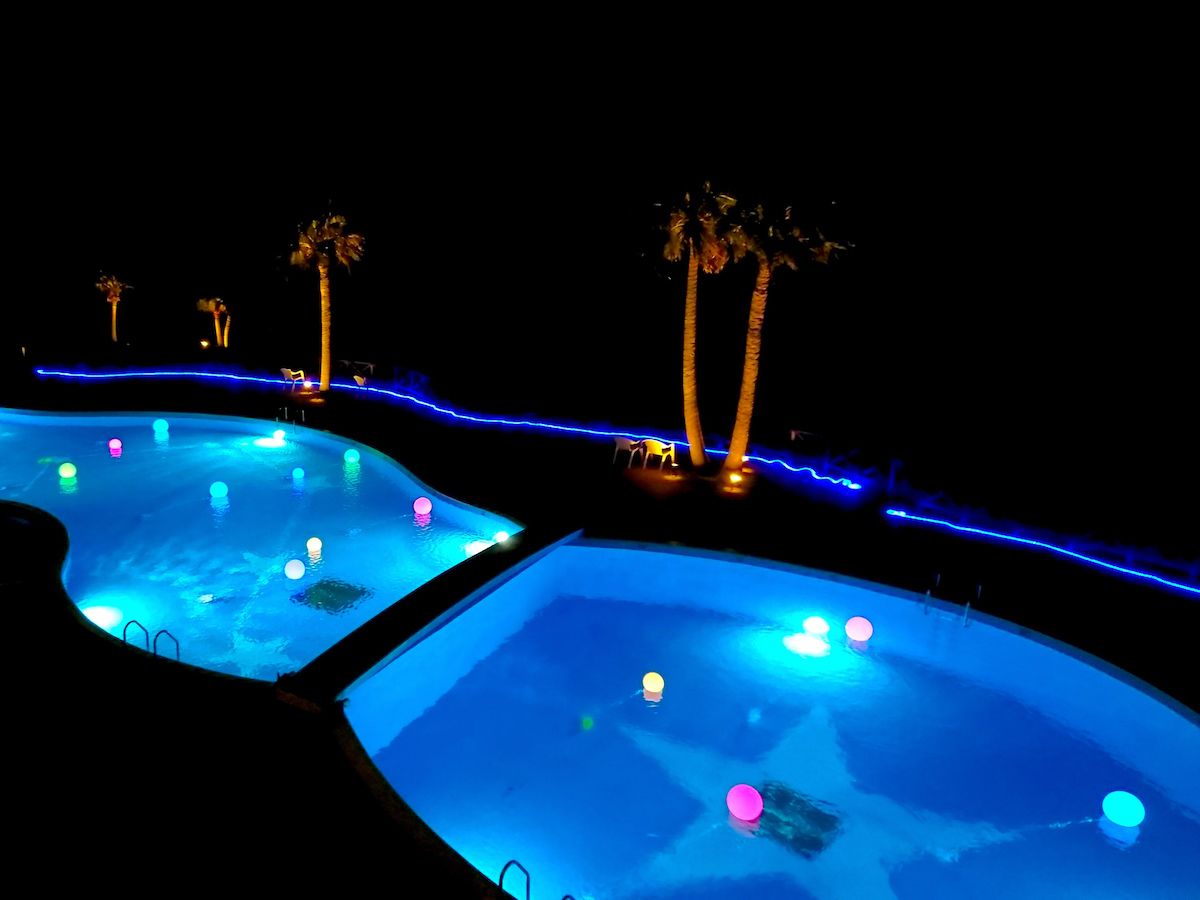 A nighttime view of a swimming pool area with two pools, palm trees, and blue ambient lighting.