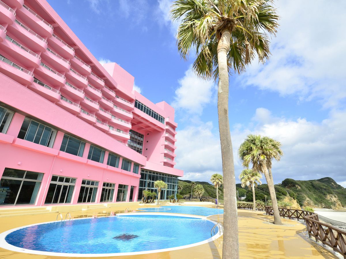 Un hôtel rose avec une piscine et des palmiers.