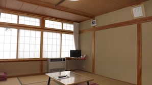 Ein traditioneller japanischer Raum mit Tatami-Böden, einer Tatami-Matte in der Mitte, einem kleinen Tisch mit Fernbedienung, einem Heizgerät und einem Fenster mit Blick.