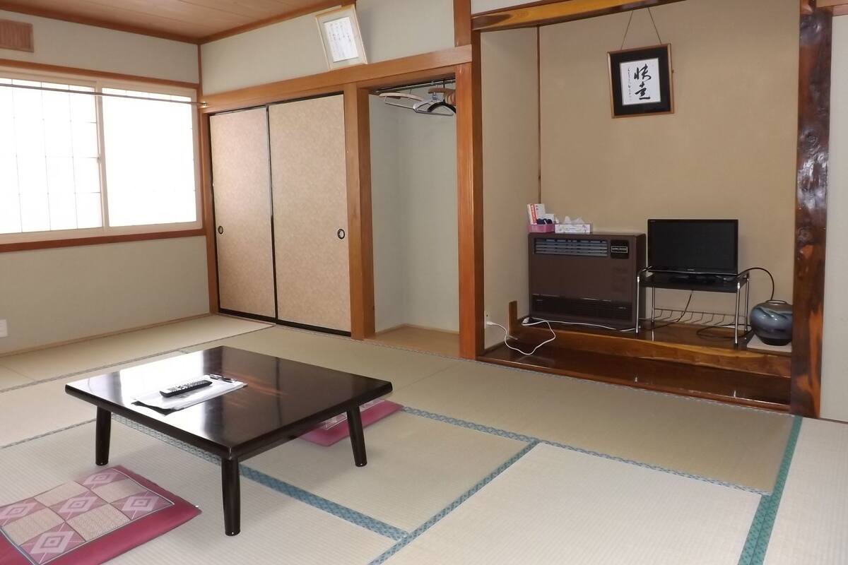 A traditional Japanese room with tatami flooring, a low table, a television on a wooden stand, and a sliding door closet.