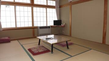 A traditional Japanese room with tatami flooring, a tatami mat table, a heater, and a television on a shelf.