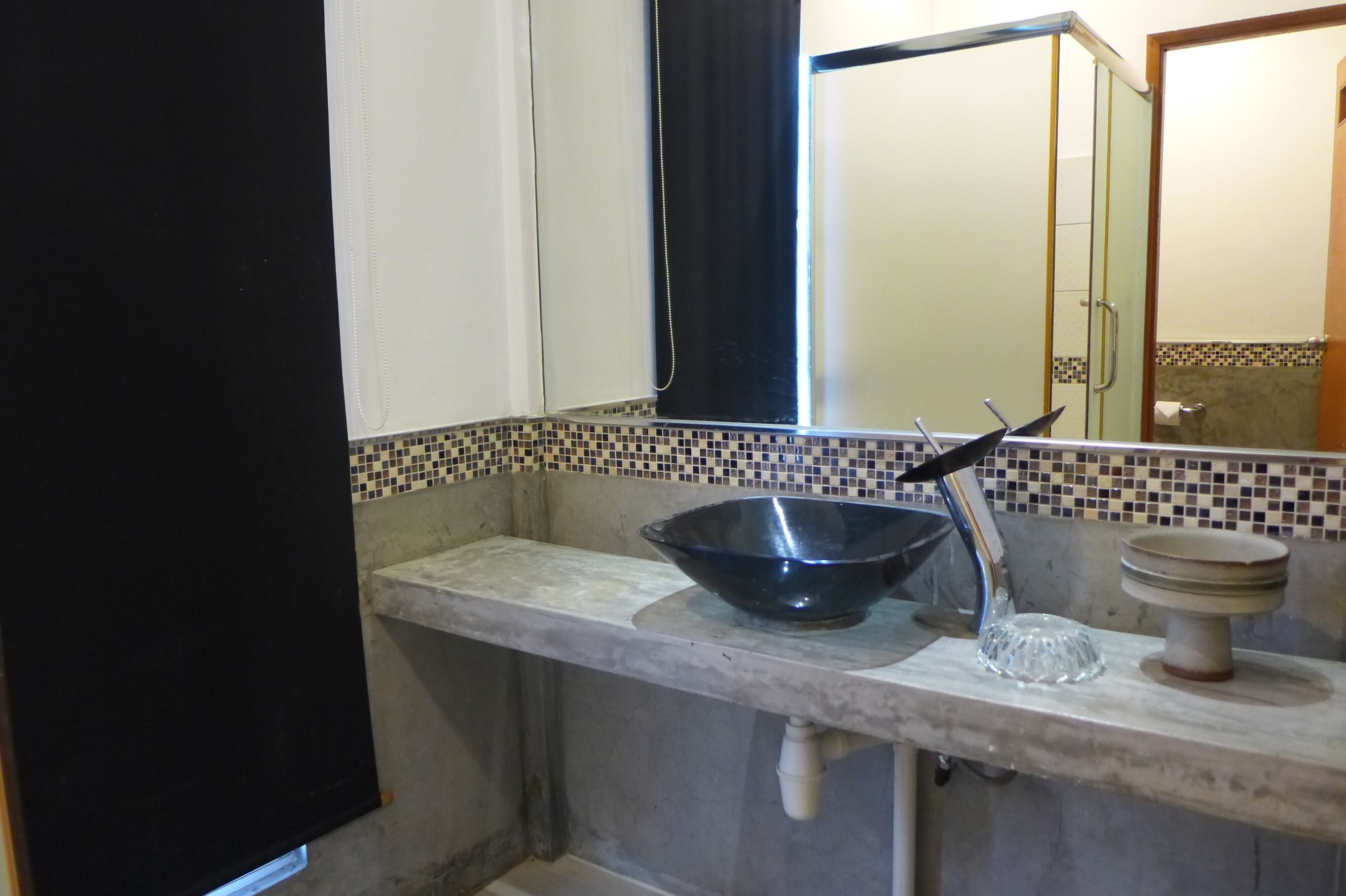 A bathroom with a tiled backsplash, a black basin, a glass bowl, and a small pedestal sink.