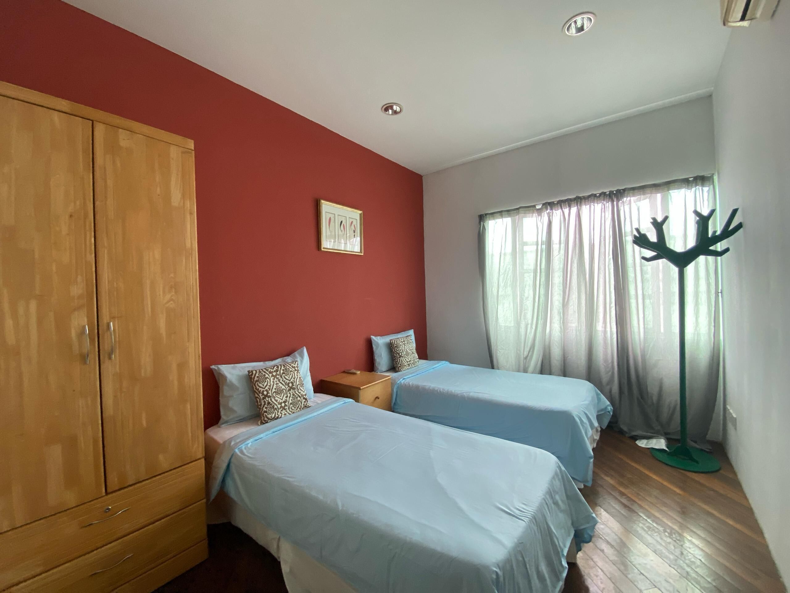A bedroom with two beds, a wardrobe, a window with curtains, and a coat rack.