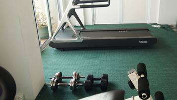 Un gimnasio con una cinta de correr, mancuernas y un banco.