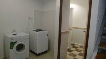 A laundry room with a front-loading washer and dryer, a small table with a lamp, and a door leading to another room.