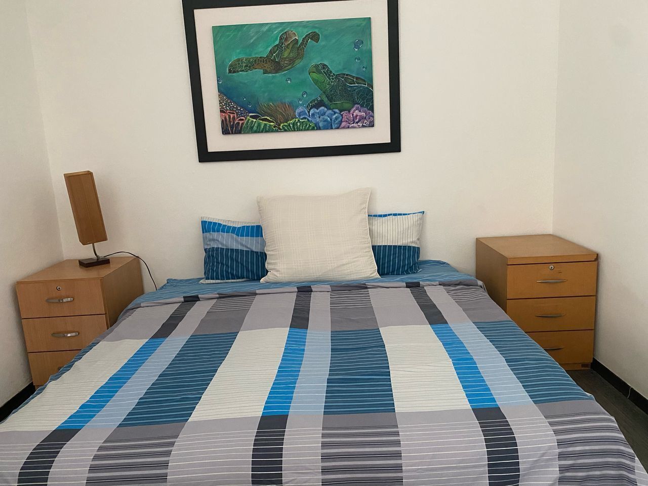 Un dormitorio con una cama, dos mesitas de noche, un cuadro enmarcado en la pared y un armario de madera.