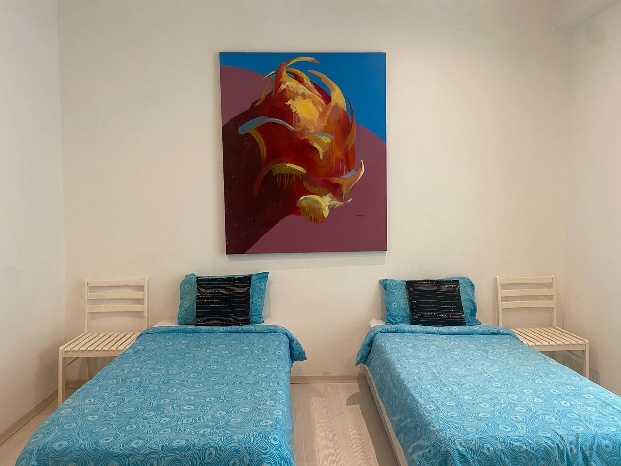 A bedroom with two single beds, each with a patterned blue bedspread and matching pillows. There is a painting on the wall above the beds.