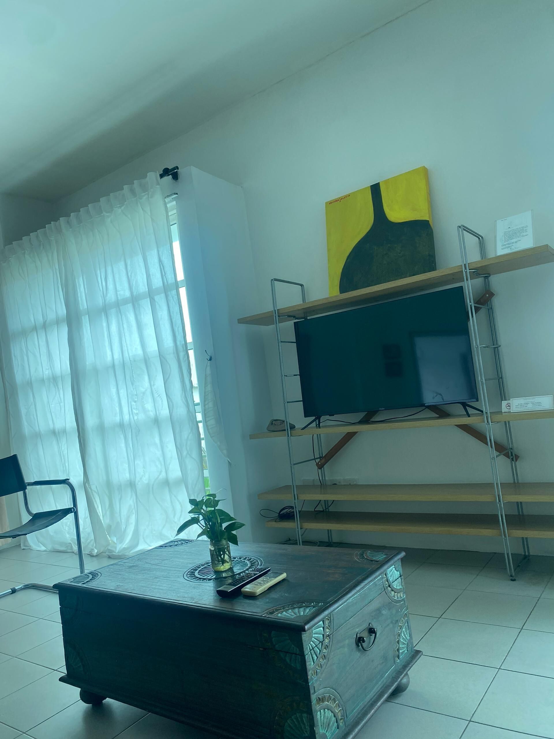 A living room with a TV on a wooden shelf, a decorative table, and a plant.