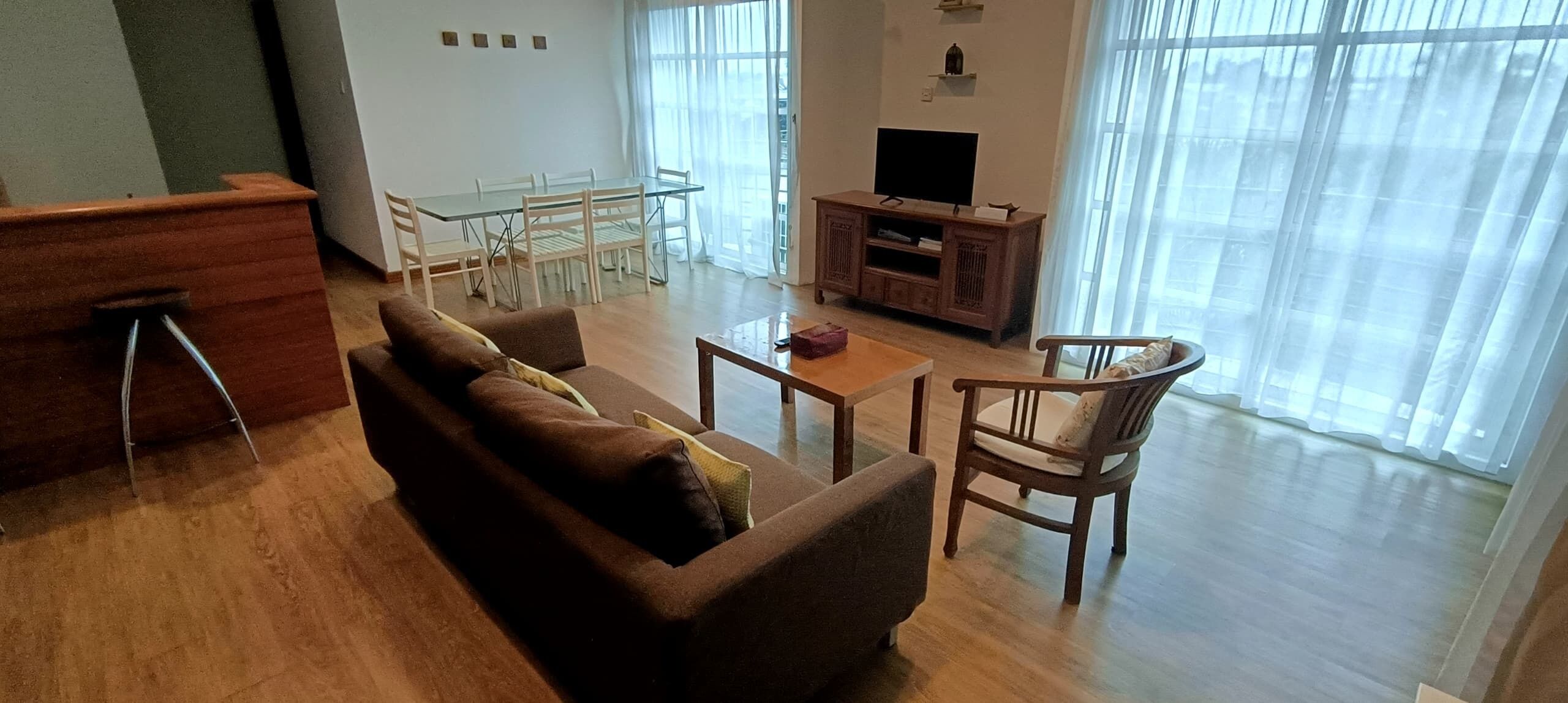A living room with a sofa, a coffee table, a TV stand, and a dining table with chairs.