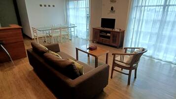 A living room with a sofa, a coffee table, a TV stand, and a dining table with chairs.