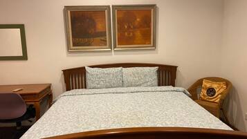 A bedroom with a wooden bed, a desk, a chair, and two framed paintings on the wall.