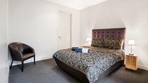 Un dormitorio con cama, una silla, mesita de noche y lámpara.