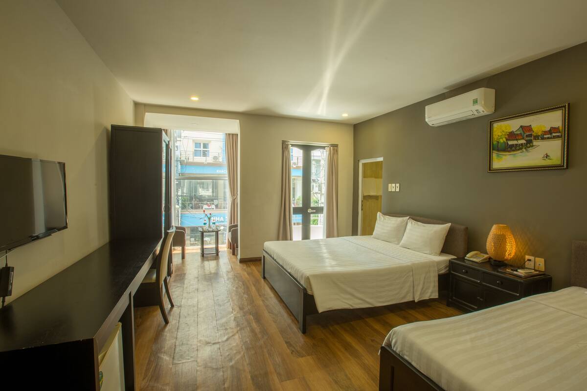A hotel room with a bed, bedside table, TV, and a view of the outside.
