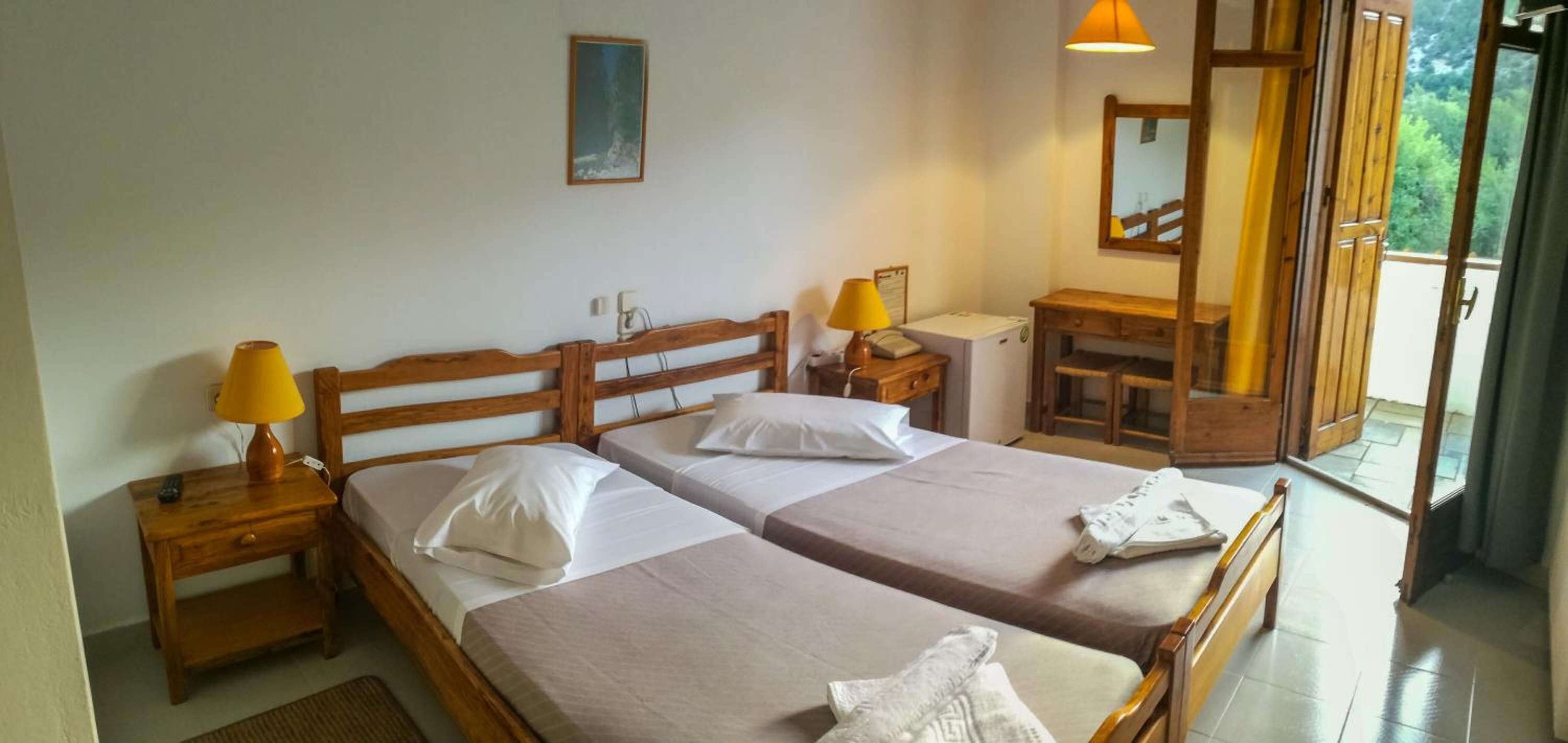 Ein Zimmer mit zwei Betten, Holz-Kopfteilen, Nachttischen mit Lampen, einem kleinen Schreibtisch und einem Spiegel.