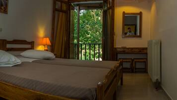 A double bed with a wooden headboard, two bedside lamps, a small table with a lamp, a mirror, and a window with a view of trees.