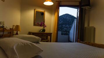 Quarto de hotel com uma cama, uma escrivaninha, um espelho, um abajur e vista para uma montanha.