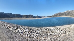 Un paysage naturel caractérisé par une étendue d’eau importante, un terrain rocheux et des montagnes en arrière-plan.