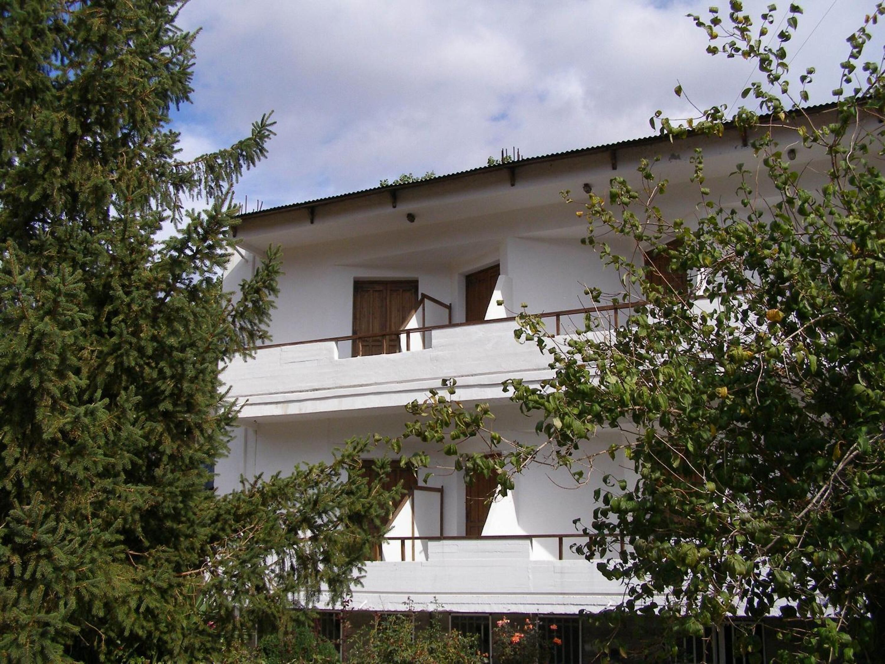 A two-story building with a balcony, surrounded by trees.