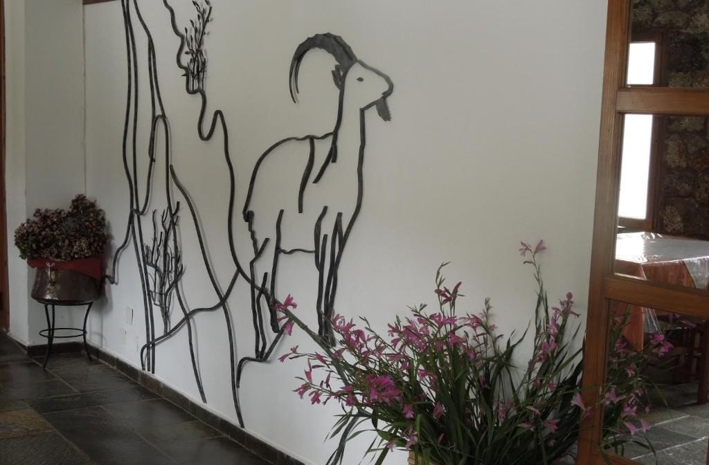 A wall with a line drawing of a goat and a human profile. There are potted plants on the floor.