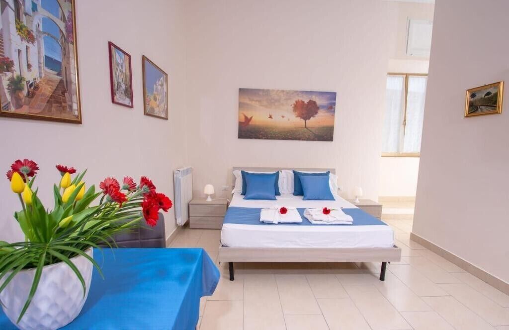 A well-lit bedroom with a bed, bedside tables, a vase of flowers, and artwork on the walls.
