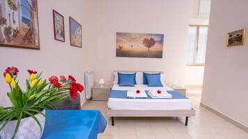 A well-lit bedroom with a bed, bedside tables, a vase of flowers, and artwork on the walls.