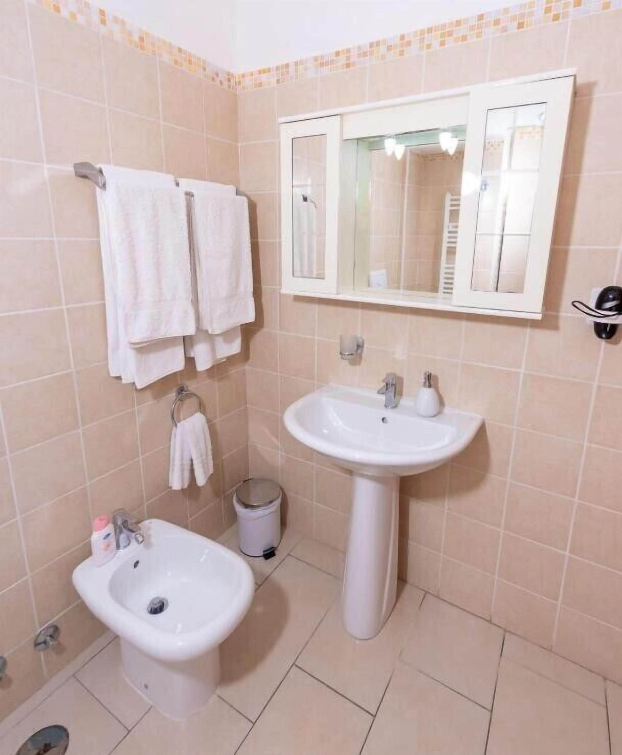 Un baño con lavamanos pedestal, un bidé y dos toallas colgadas en un perchero.
