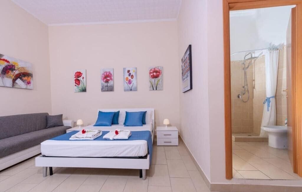 A bedroom with a bed, a grey sofa, and a shower area visible through an open door.