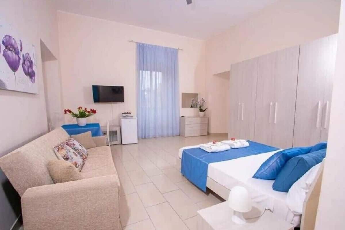 Ein Hotelzimmer mit Bett, Sofa, Fernseher, Schreibtisch und Kleiderschrank.