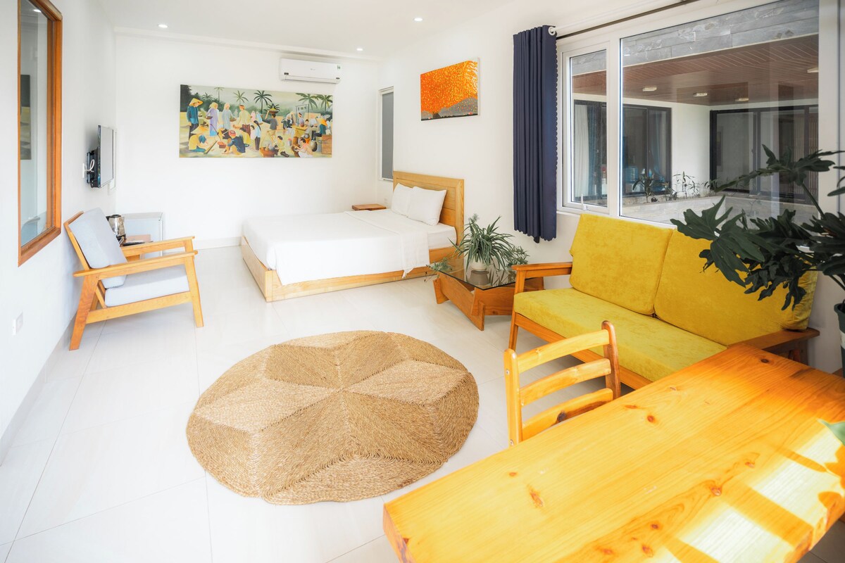 A room with a bed, a sofa, a dining table, a small rug, and a potted plant.