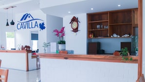 A modern hotel lobby with a reception desk, a clock, and a sign that reads "CAVILLA".