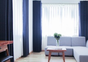 A modern living room with a grey sofa, a wooden coffee table with a vase of flowers, and dark curtains. - Cavilla Hotel & Apartment (Da Nang)