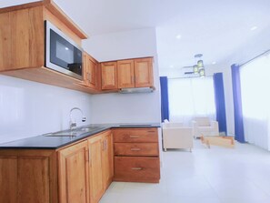 A modern kitchen with wooden cabinets, a microwave, and a sink. There is a dining area with a white table and chairs.