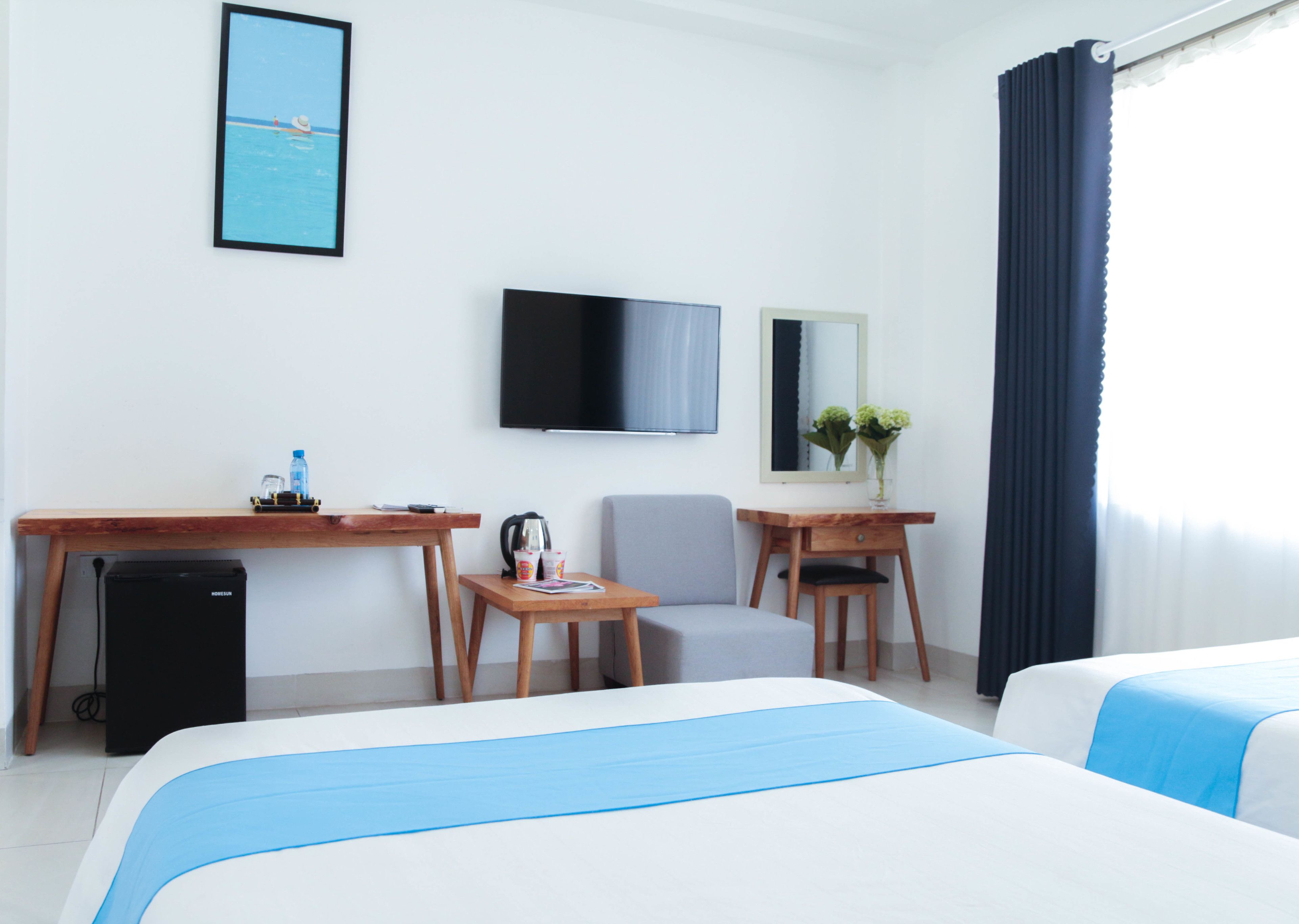 A hotel room with a bed, a desk, a chair, a television, a small table with a vase of flowers, and a window with curtains.