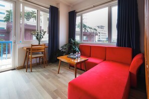 Een kamer met een houten stoel, een klein tafeltje, een rode bank en een bloempot met plant.