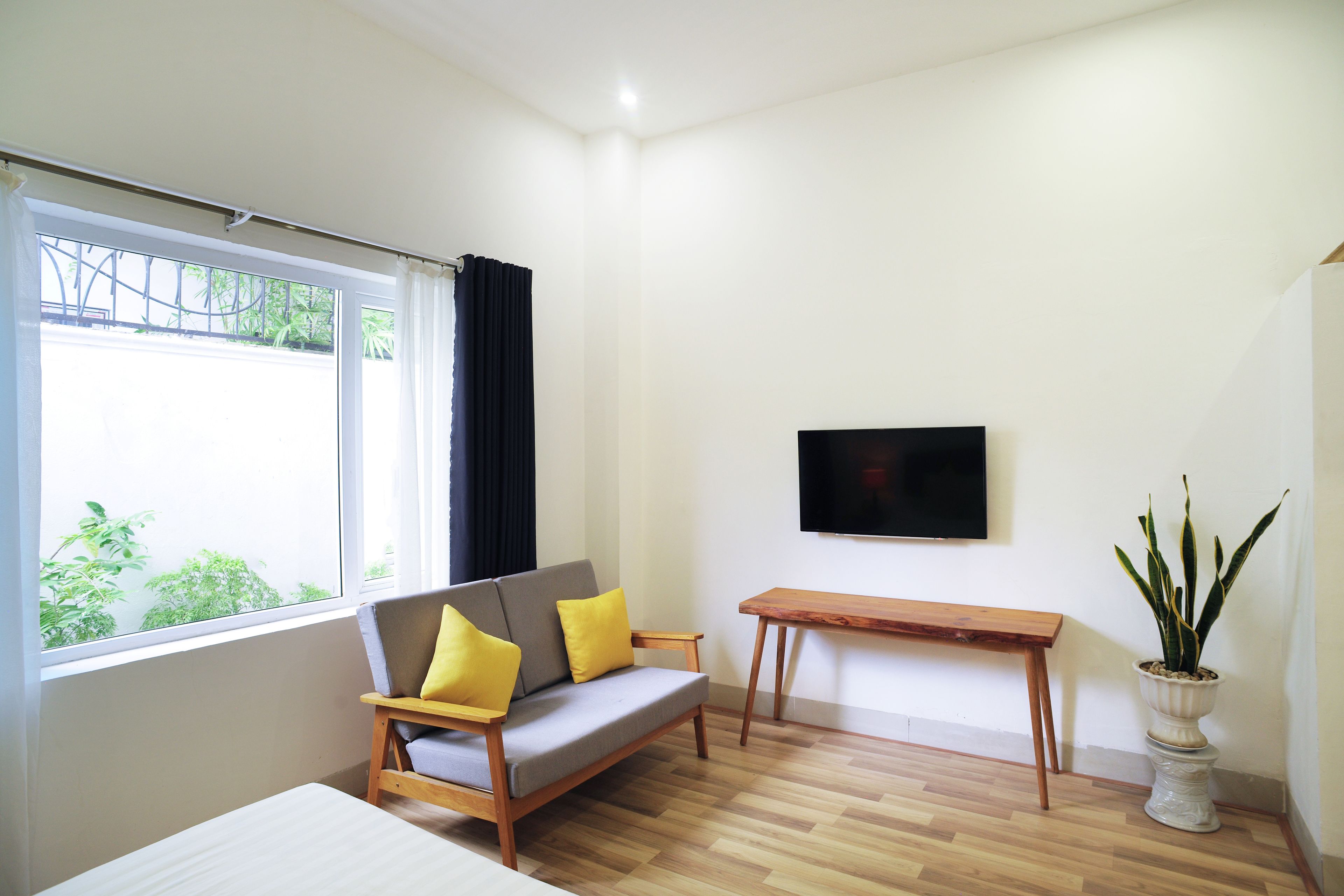 Una sala de estar moderna con un sofá, una mesa de madera, un televisor montado en la pared y una planta en maceta.
