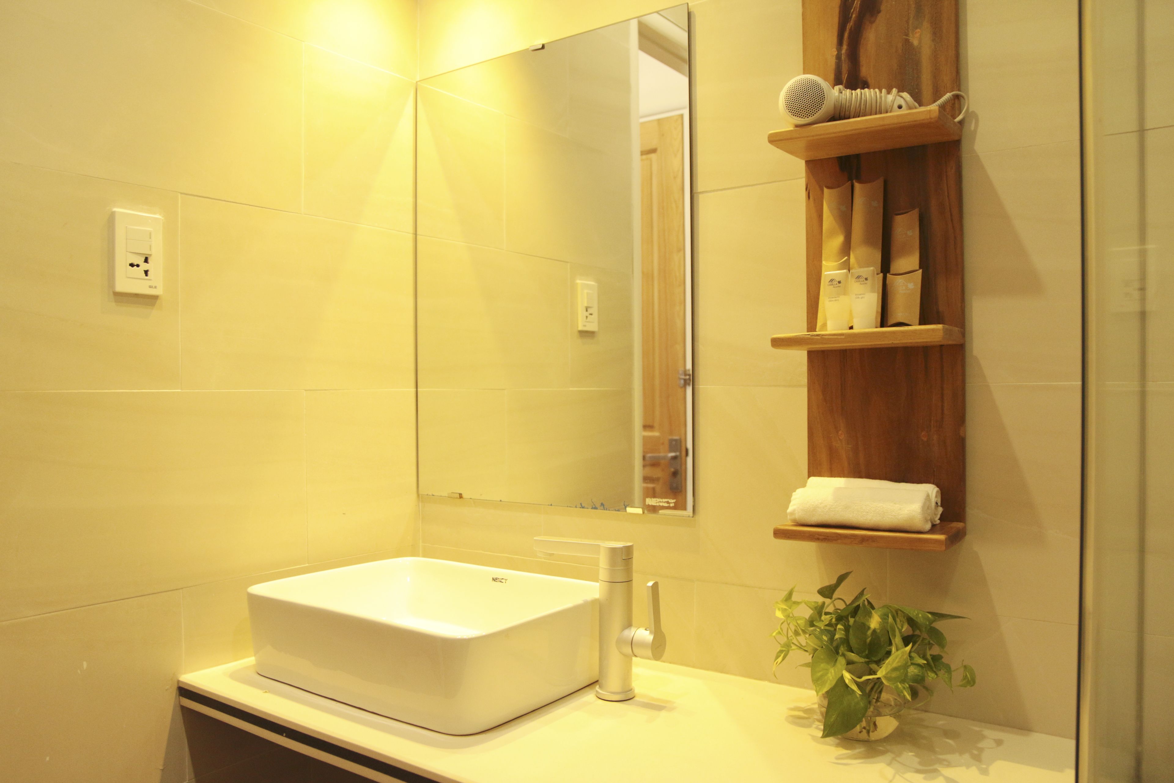 Un baño con un lavabo blanco, un espejo, un perchero para toallas y un estante con artículos de aseo.